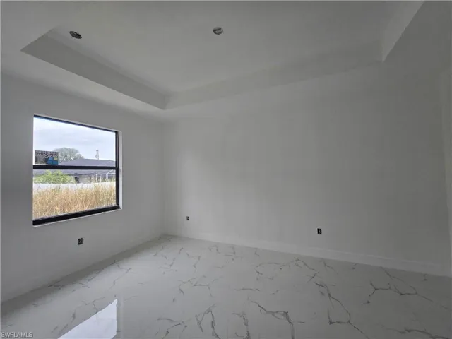 Empty room featuring light marble finish floors and a tray ceiling