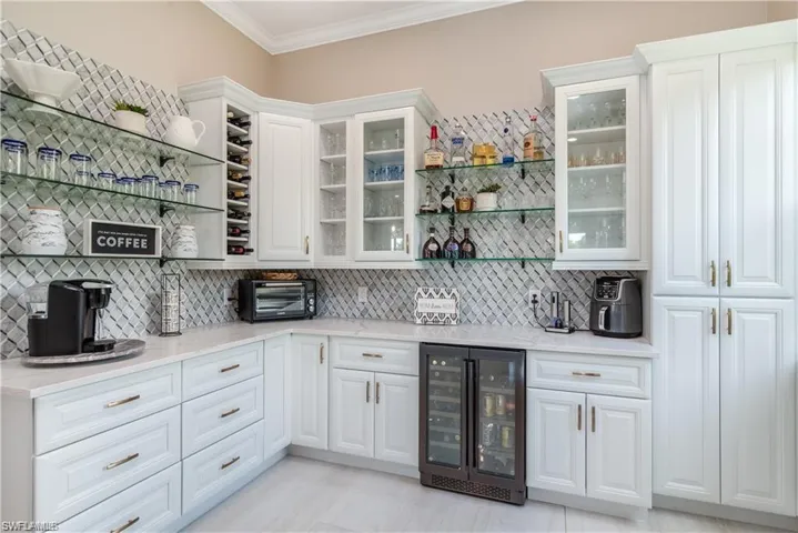 Bar area with open shelves, beverage cooler, ornamental molding, glass insert cabinets, and light stone counters