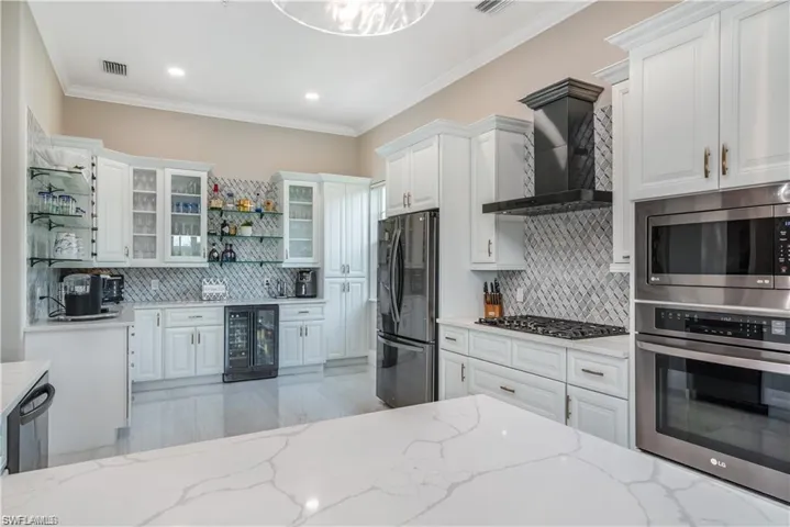 Kitchen featuring white cabinetry, stainless steel appliances, open shelves, glass insert cabinets, and wall chimney range hood