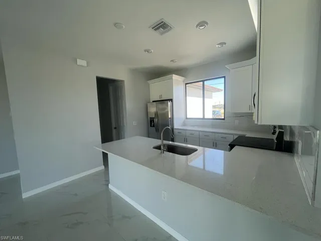 Kitchen with white cabinets, sink, kitchen peninsula, stainless steel fridge with ice dispenser, and black stove