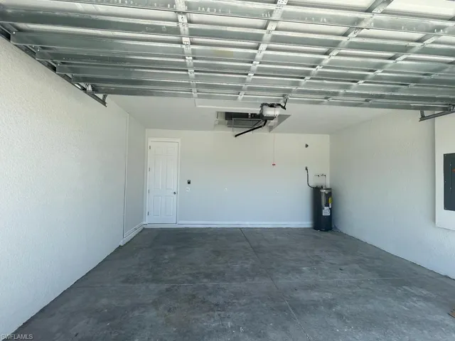 Garage with electric water heater, electric panel, and a garage door opener