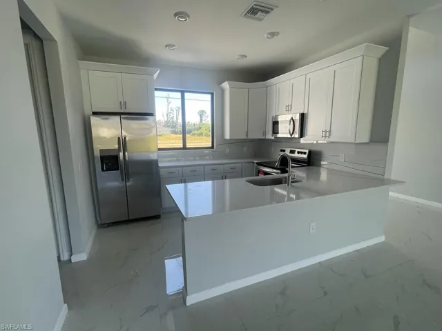 Kitchen with kitchen peninsula, white cabinetry, sink, and stainless steel appliances