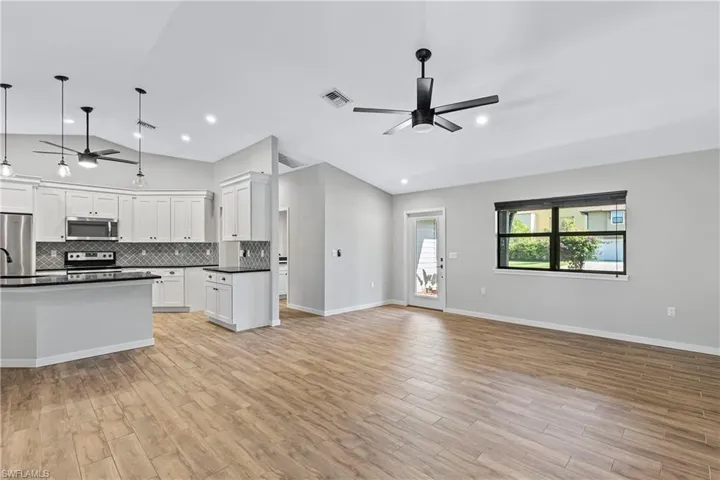 Kitchen with appliances with stainless steel finishes, decorative light fixtures, light hardwood / wood-style flooring, white cabinetry, and lofted ceiling