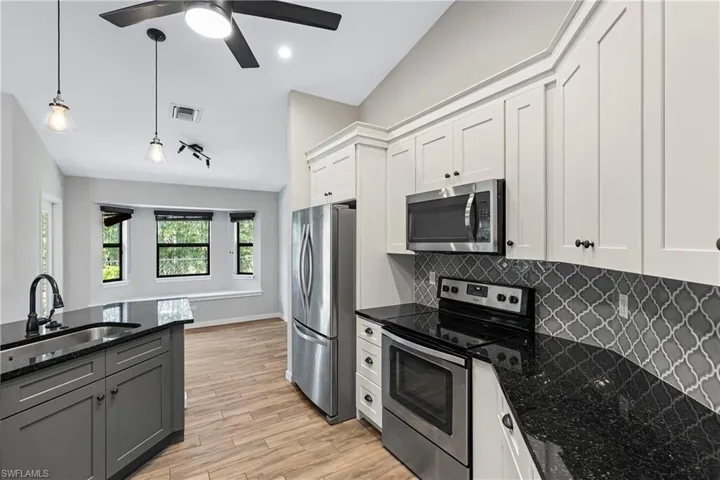Kitchen with dark stone countertops, white cabinetry, stainless steel appliances, and vaulted ceiling