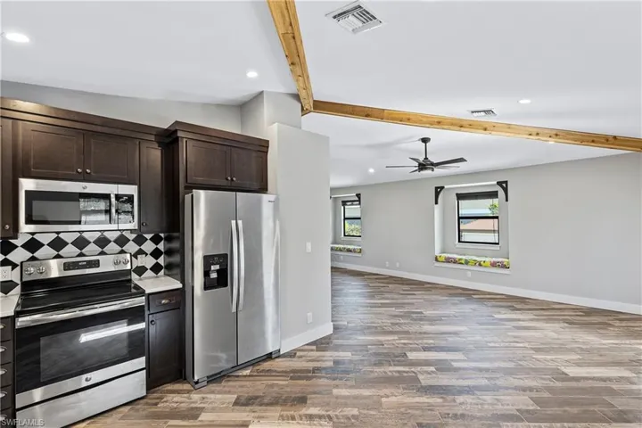 Kitchen featuring decorative backsplash, appliances with stainless steel finishes, dark brown cabinets, beam ceiling, and hardwood / wood-style floors