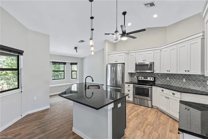 Kitchen with appliances with stainless steel finishes, sink, light hardwood / wood-style floors, white cabinetry, and lofted ceiling