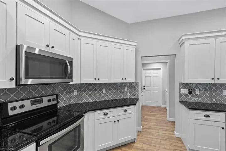Kitchen with decorative backsplash, light wood-type flooring, stainless steel appliances, dark stone countertops, and white cabinetry