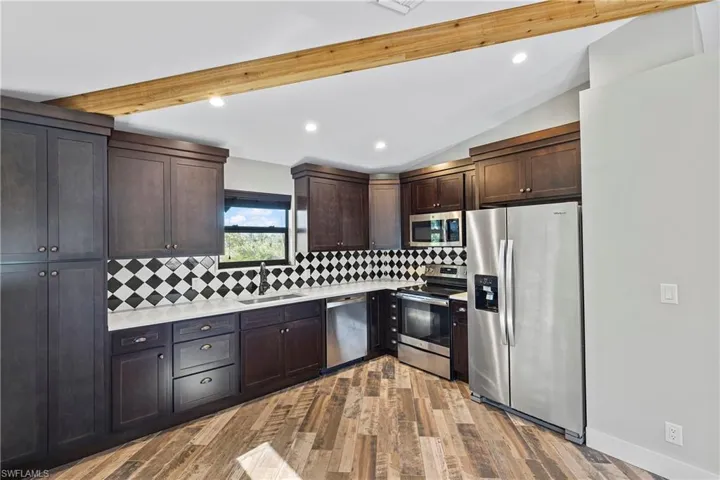 Kitchen with lofted ceiling with beams, sink, appliances with stainless steel finishes, tasteful backsplash, and light hardwood / wood-style floors