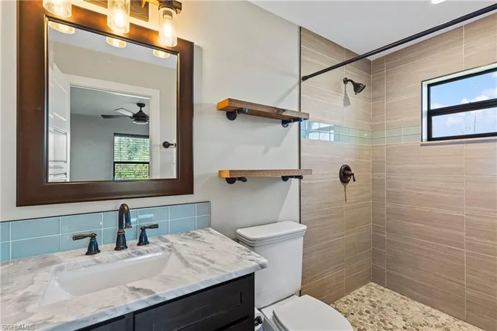 Bathroom featuring a tile shower, toilet, ceiling fan, and a healthy amount of sunlight