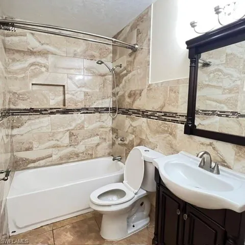 Bathroom featuring a tiled shower surround with an accent mosaic band, an integrated shower niche, a white bathtub, and a dark wood-finish vanity with an integrated sink