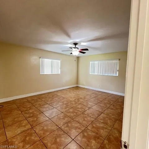 Spacious room featuring tile flooring, two windows with horizontal blinds, and a ceiling fan with integrated lighting