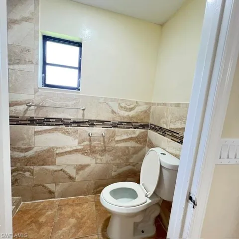 Bathroom featuring tile flooring and walls, a window, and a standard toilet