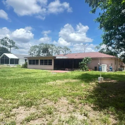 Spacious rear yard with a neutral-toned exterior, sunroom, screened patio, and mature trees providing shade