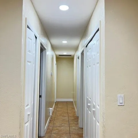 Hallway featuring recessed lighting, paneled doors, neutral wall tones, and tiled flooring