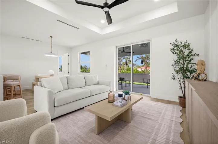 Spacious living area featuring a tray ceiling with a ceiling fan, light-toned flooring, and direct access to an outdoor patio through sliding glass doors
