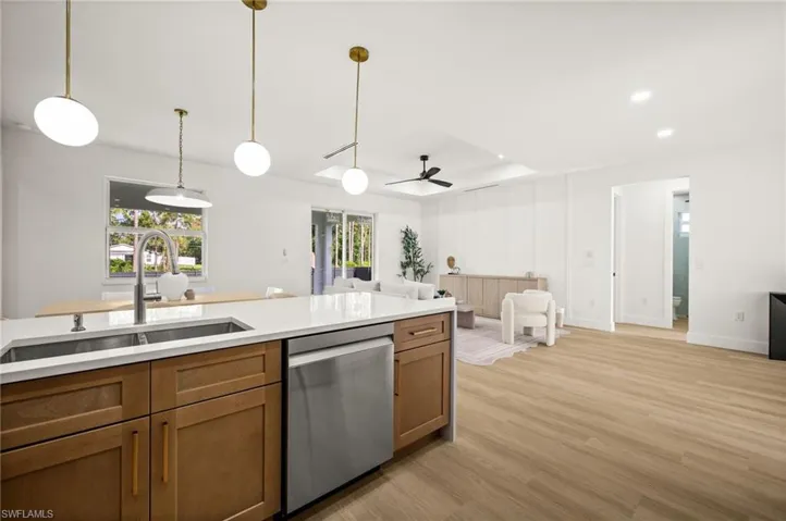 The open concept layout features a kitchen island with a double basin sink and a stainless steel dishwasher, along with recessed lighting and light wood-style flooring throughout the living areas