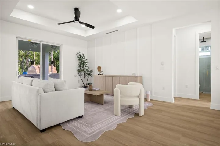 Spacious living area featuring light-toned wood style flooring, a tray ceiling with recessed lighting and a ceiling fan, and sliding glass doors that open to an outdoor view
