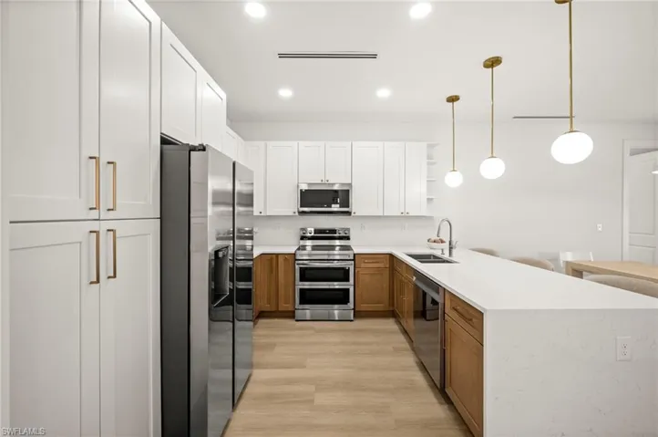 Modern kitchen featuring stainless steel appliances, white upper cabinets, natural wood lower cabinets, and a long white countertop with a sink