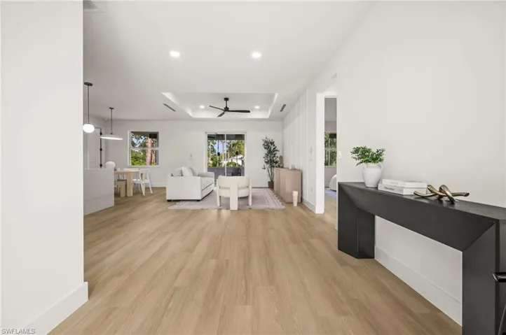 Spacious open-concept living area featuring light-toned wood style flooring, recessed lighting, and a tray ceiling with a ceiling fan