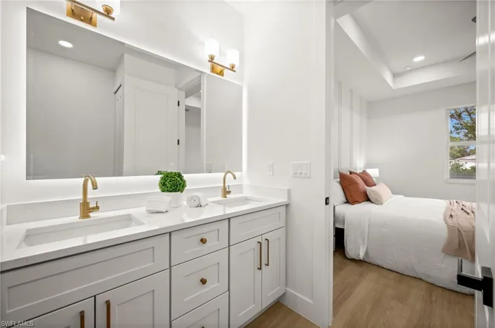 The bathroom features a dual vanity with white countertops, gold-toned faucets, and a large illuminated mirror