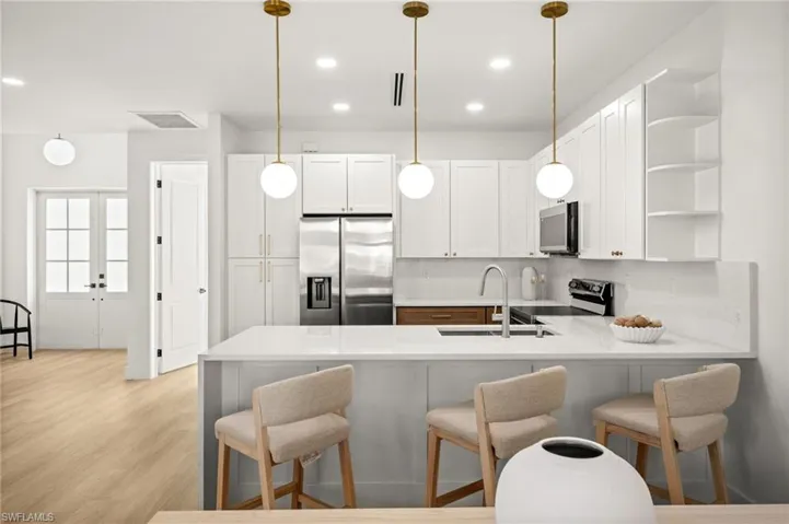 The kitchen features white cabinetry, a large kitchen island with seating, pendant lighting, and stainless steel appliances