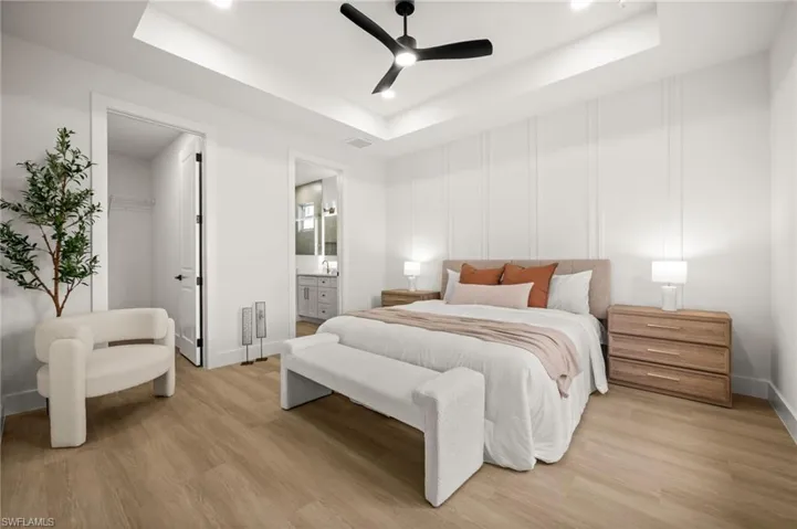 Bedroom featuring light wood-style flooring, a tray ceiling with a black ceiling fan, and wall paneling detail