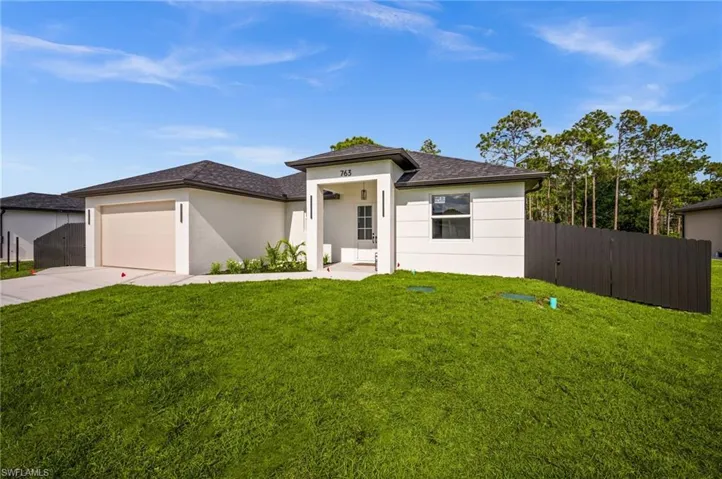The property features a well-maintained lawn and a private fence, with exterior lighting fixtures illuminating the front facade