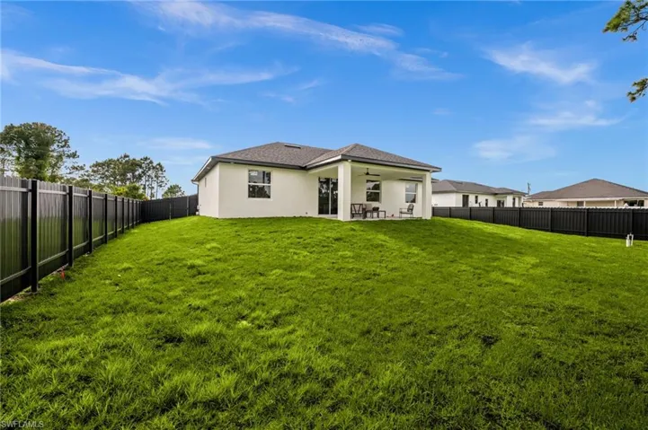 The property features an extensive lawn area, a black privacy fence, and a covered patio at the rear