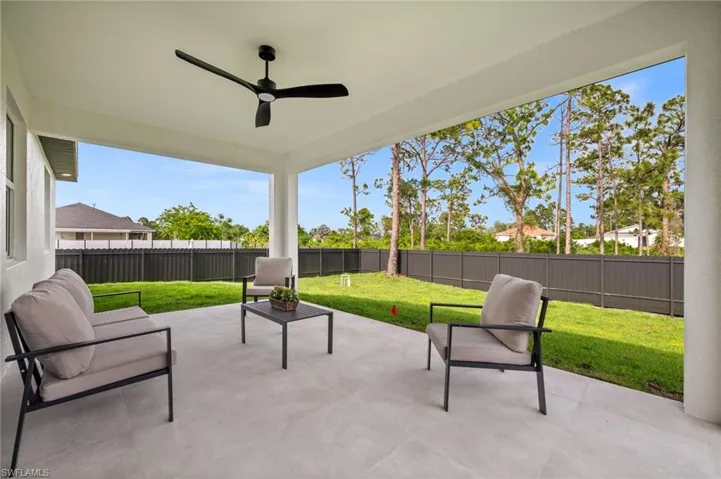 Expansive covered patio featuring a ceiling fan, tiled flooring, and views of the fenced backyard with a lawn and mature trees