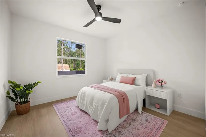 This room features light-toned wood style flooring, a window offering views of trees, and a ceiling fan with integrated lighting