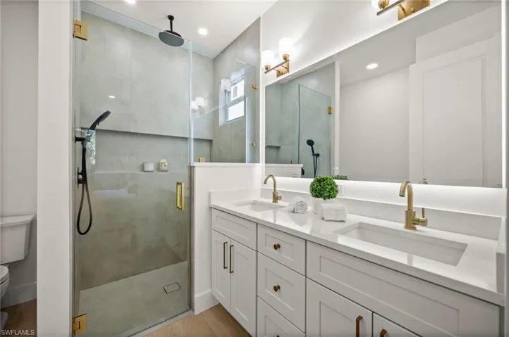 Bathroom featuring a double vanity with white cabinetry, gold fixtures, and a spacious glass-enclosed shower with a rainfall showerhead