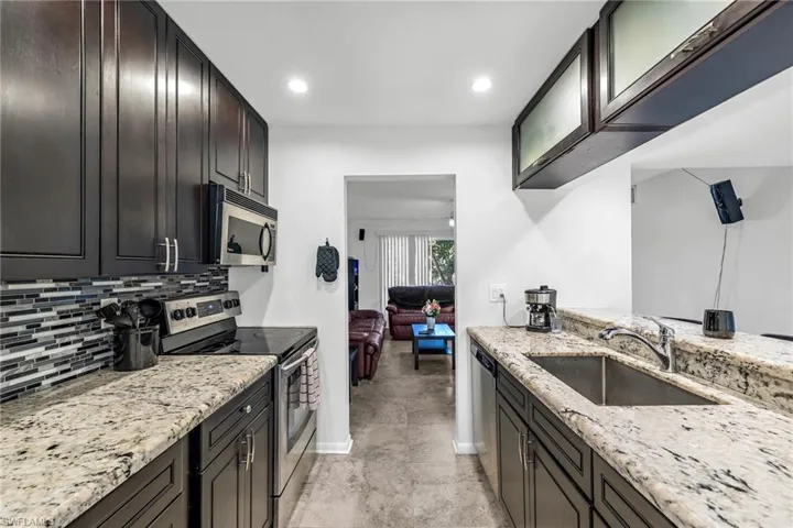 Kitchen with appliances with stainless steel finishes, light stone counters, tasteful backsplash, glass insert cabinets, and recessed lighting