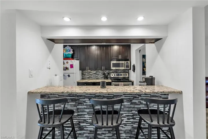 Kitchen featuring a breakfast bar, backsplash, appliances with stainless steel finishes, and light stone countertops