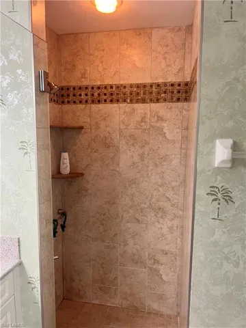 Bathroom with tiled shower, wallpapered walls, and vanity
