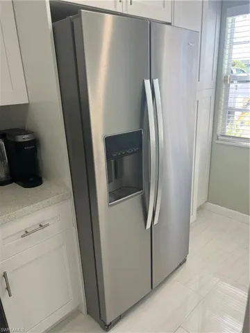 Kitchen with stainless steel fridge, white cabinets, light tile patterned floors, and light stone countertops