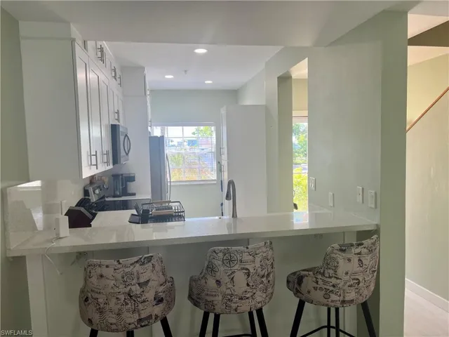 Kitchen with a peninsula, light countertops, stainless steel microwave, freestanding refrigerator, and range with electric cooktop