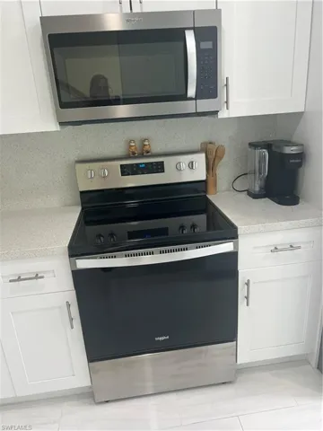 Kitchen featuring stainless steel range with electric cooktop, white cabinetry, and light stone counters