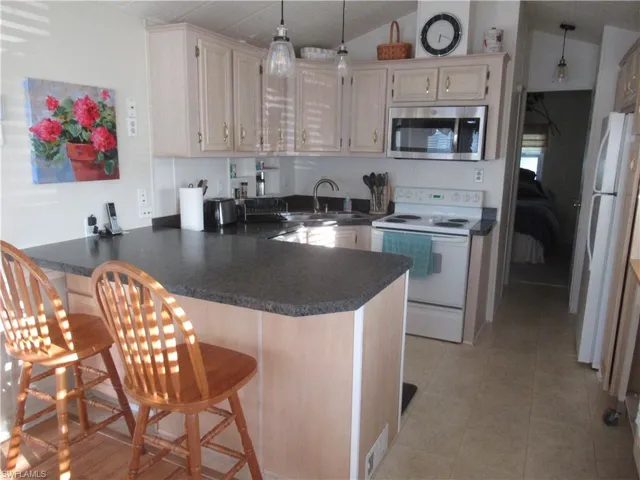 Kitchen featuring white appliances, a kitchen bar, a peninsula, dark countertops, and vaulted ceiling