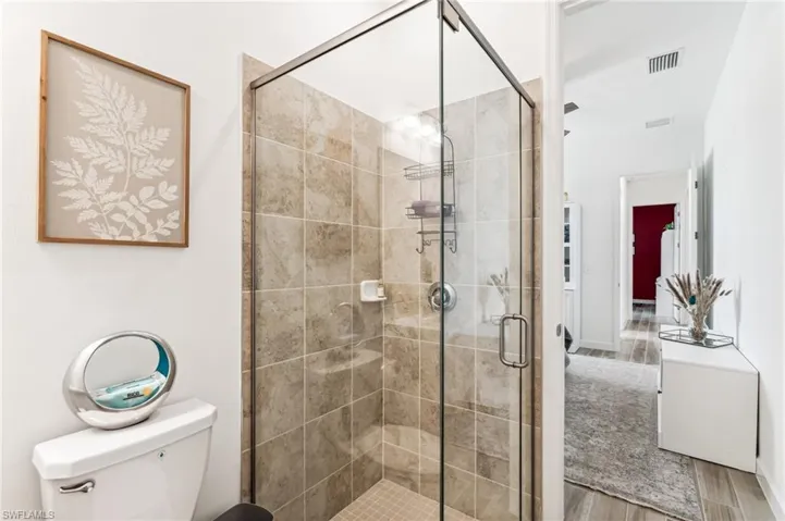Bathroom with toilet, an enclosed shower, and hardwood / wood-style floors