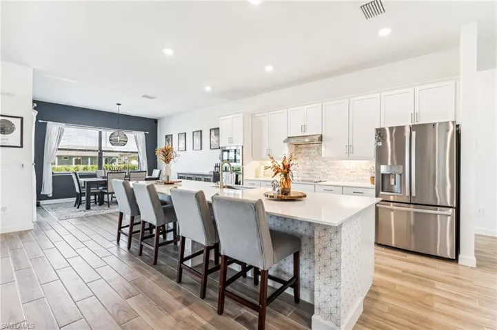 Kitchen featuring a center island with sink, white cabinetry, appliances with stainless steel finishes, light wood-type flooring, and pendant lighting