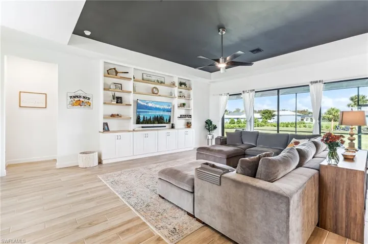 Living room featuring light wood-type flooring, ceiling fan, and a raised ceiling