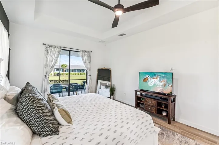 Bedroom featuring access to outside, hardwood / wood-style floors, ceiling fan, and a raised ceiling