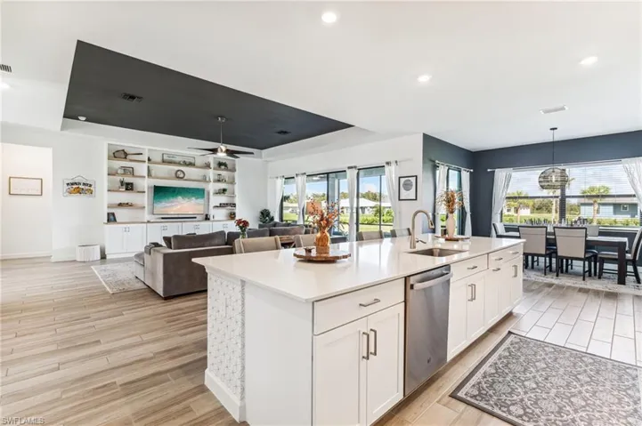 Kitchen featuring a center island with sink, white cabinets, sink, stainless steel dishwasher, and light hardwood / wood-style flooring