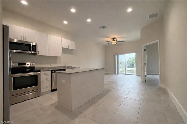 Kitchen featuring appliances with stainless steel finishes, a kitchen island, recessed lighting, light stone countertops, and light tile patterned floors