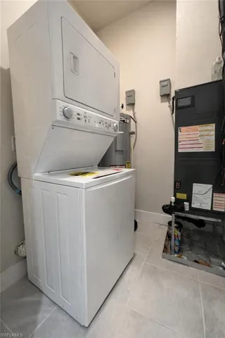 Laundry room featuring heating unit, light tile patterned floors, and stacked washer / drying machine