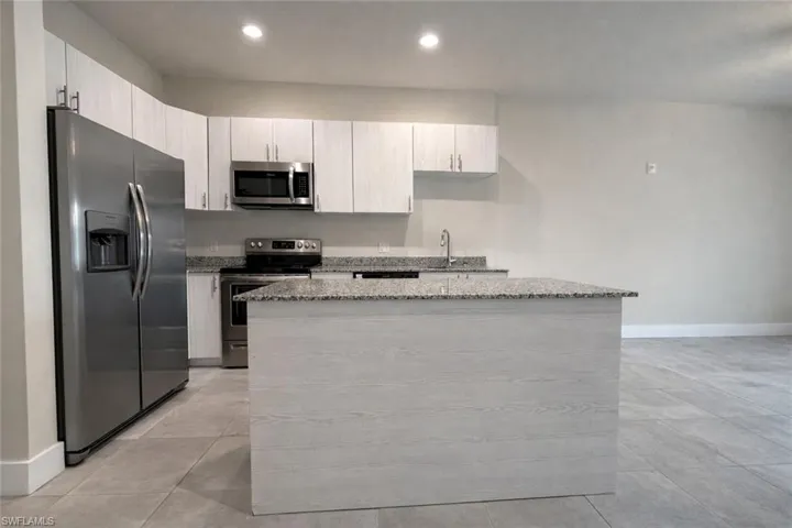 Kitchen featuring stainless steel appliances, light stone countertops, a center island, and recessed lighting