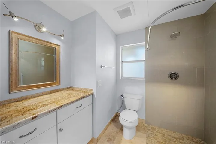 Bathroom featuring a vanity with a stone countertop, white cabinetry, and a framed mirror