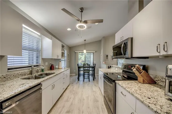Kitchen with a ceiling fan, vaulted ceiling, white cabinets, and newer appliances with graphite colored  finishes