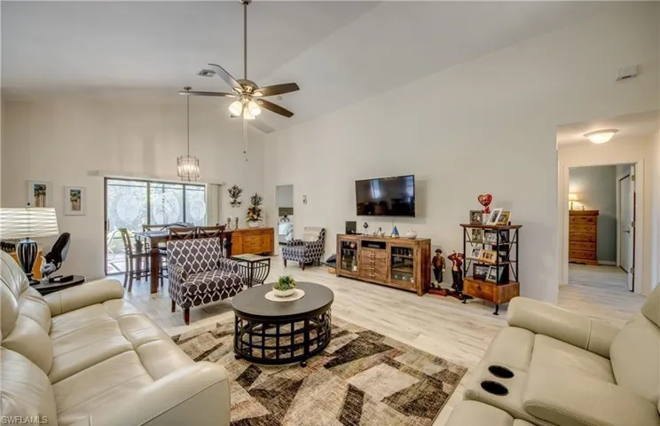 Living room featuring high vaulted ceiling, and ceiling fan. Hallway leading to spare bedroom, bathroom and den in the background