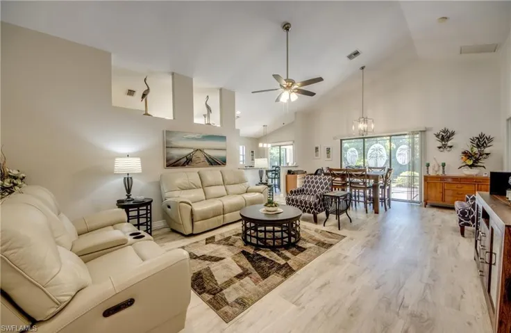 Living room featuring visible vents, ceiling fan with notable chandelier, high vaulted ceiling, and light wood-style floors
